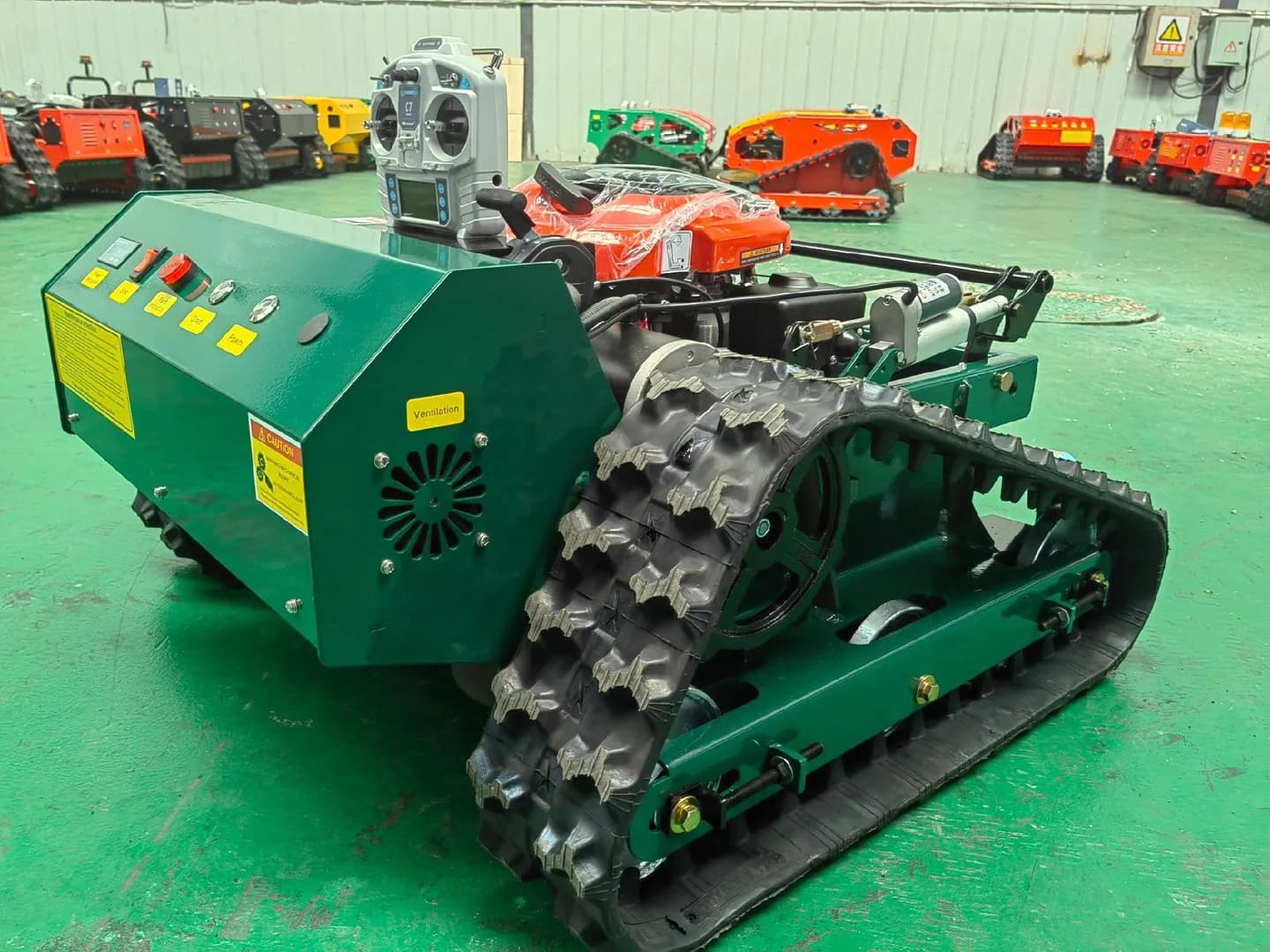 Green tracked mower with a remote controller on its control housing